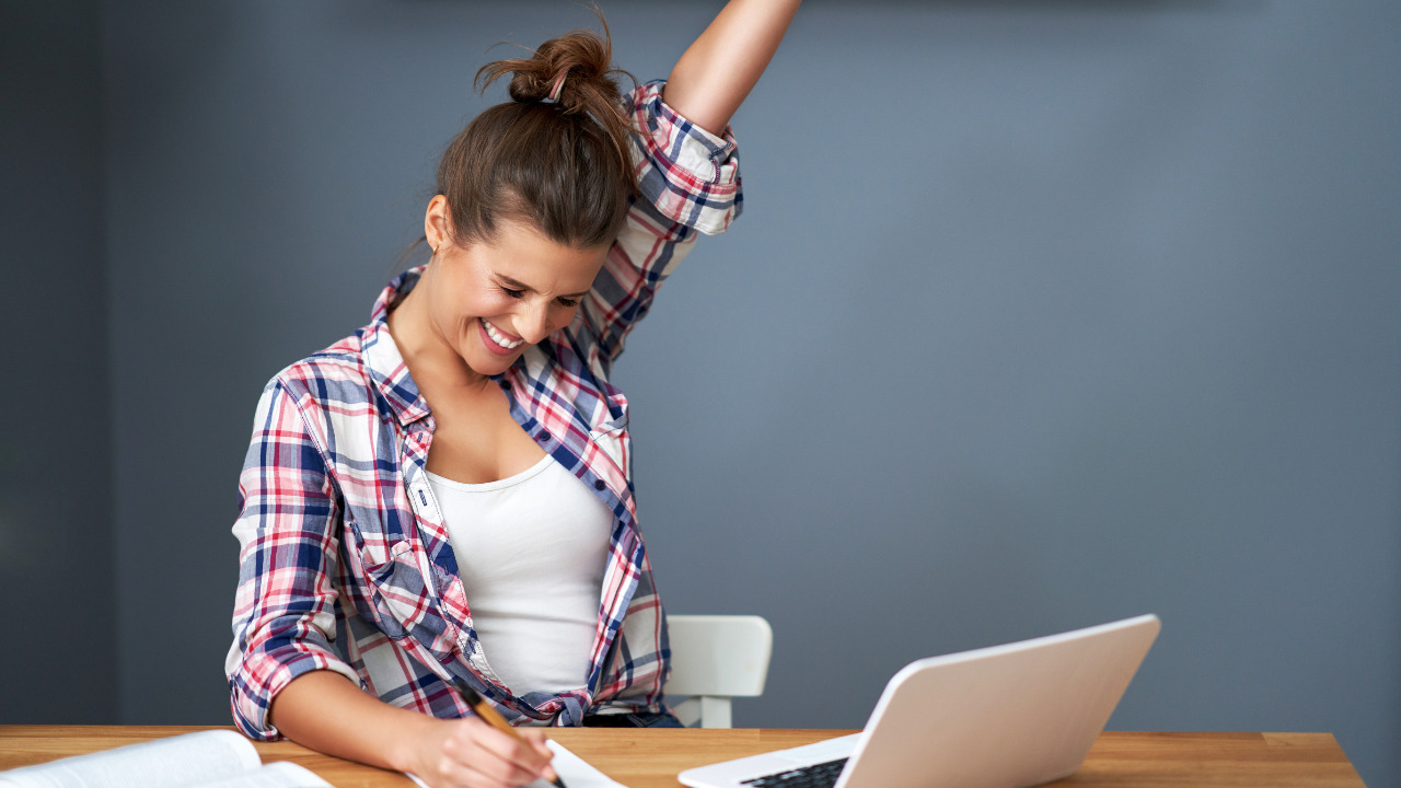 Frau freut sich über ihren Erfolg in der Erwachsenenbildung und jubelt vor ihrem Laptop