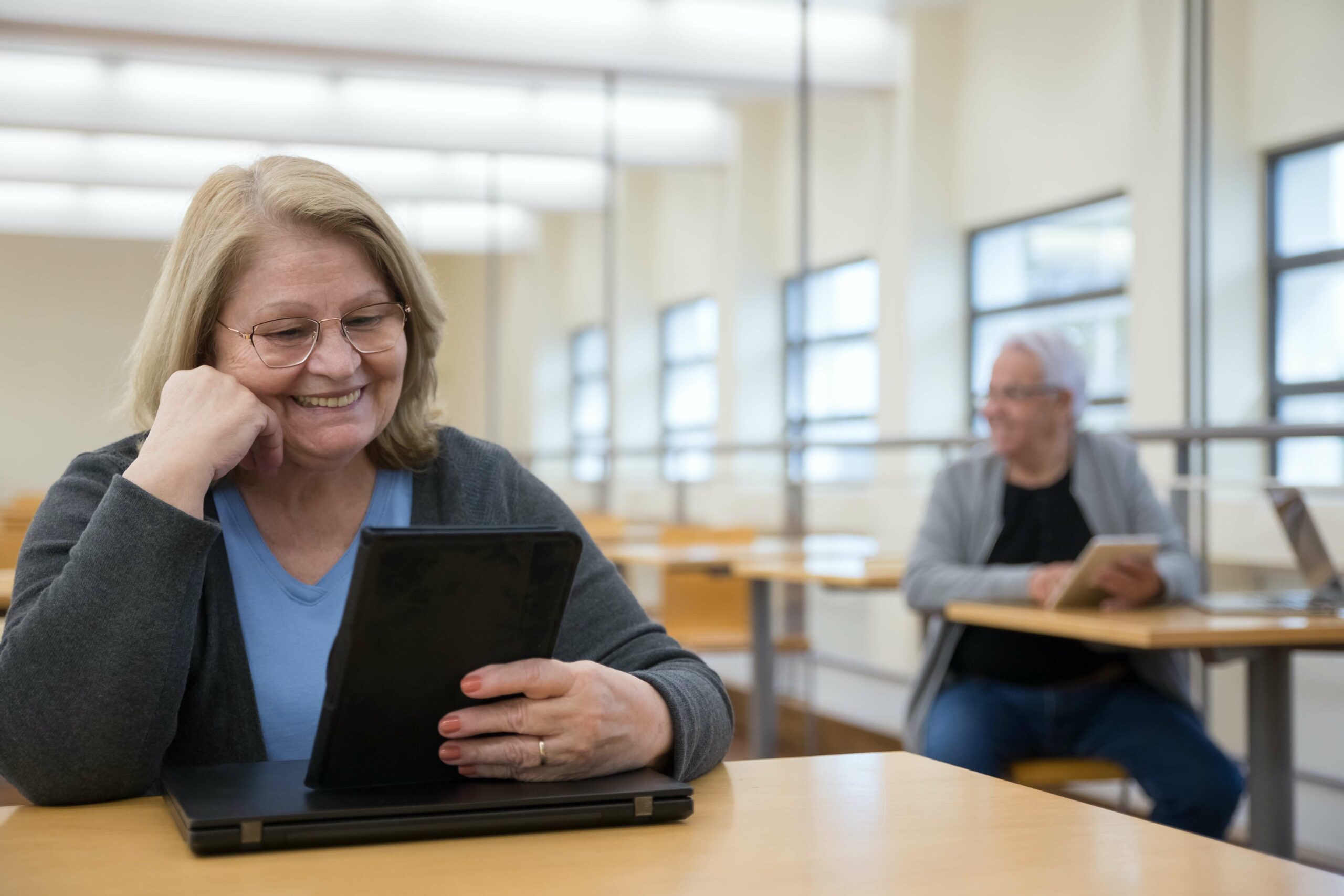 Ältere Dame hält Tablet in der Hand und lernt in Klassenzimmer