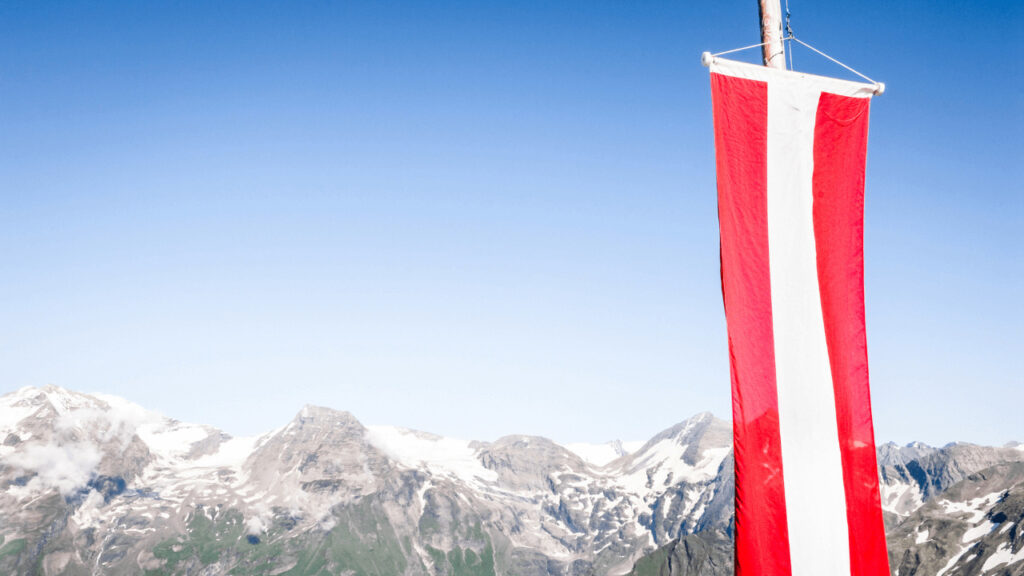Österreich-Flagge weht vor Gebirgskette im Hintergrund